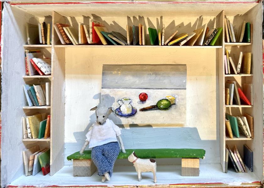 Frank and Rudy by Virginia McCracken A detailed miniature diorama of a cozy room with built-in bookshelves filled with small colorful books. In the center, a mouse figurine wearing a white sweater and blue skirt sits on a green bench, with a small white dog standing beside it. Behind them hangs a tiny still-life painting of a pitcher, fruit, and a knife on a table, adding to the handcrafted, storybook feel of the scene.