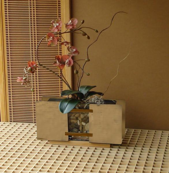 Linn Vase #6 by Warren Yip Modern floral arrangement with pink orchids in a decorative vase filled with stones on a textured tabletop.