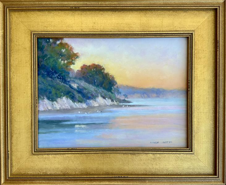 Awakening by Linda Mutti Framed coastal landscape painting of a calm shoreline with cliffs, trees, and pastel sunset reflections on the water