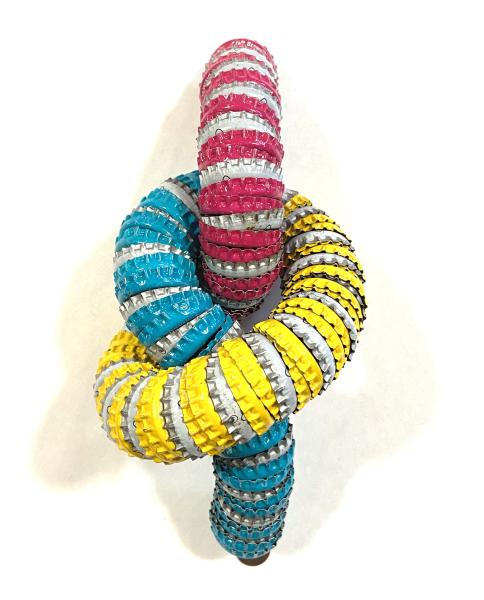 Love Me Knot by Dan Levin Colorful wall sculpture made from painted metal bottle caps arranged in interlocking loops of pink, yellow, and blue.
