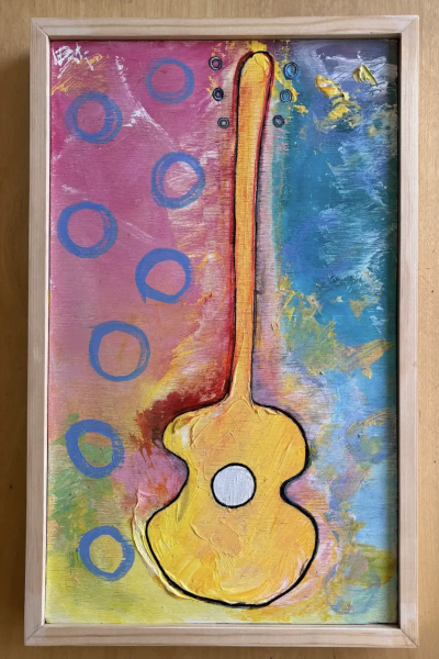 Post Winter Solo by Steve Shelton is a colorful mixed-media painting of a stylized yellow guitar outlined in black, centered vertically on a textured background split between pink with blue circles on the left and blue-green tones on the right, all framed in light wood.