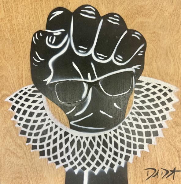 RGB Protest Fist by David Diamant Black raised fist wearing glasses with a white lace collar stencil painted on a wooden background.
