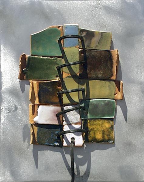 Wall-mounted mixed-media sculpture composed of layered ceramic and metal tiles in earthy green, brown, cream, and gold tones, bound together with black metal rings against a textured gray background.